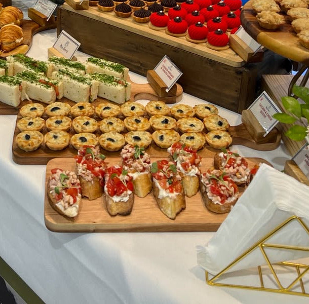 Cucumber sandos, mini quiches and bruschetta on wooden boards at a Mrs Kaur’s event table