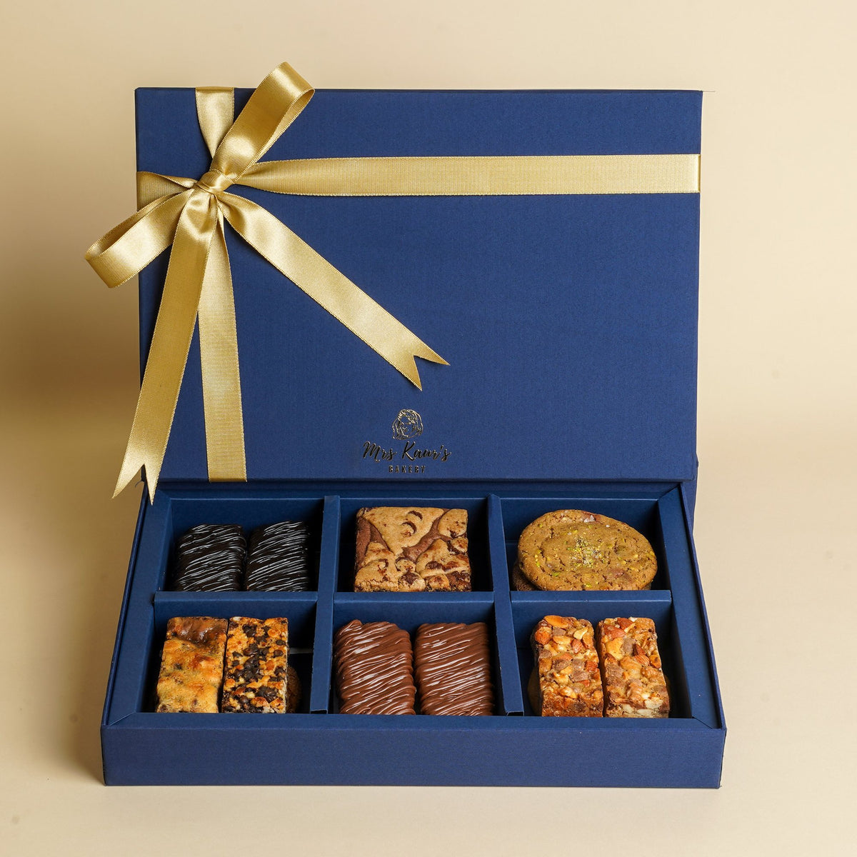An open navy Mrs Kaur’s gift box tied with gold ribbon, filled with brownies, bars, and cookies