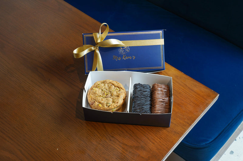 A cookie and brownies in a Mrs Kaur’s box on a walnut table