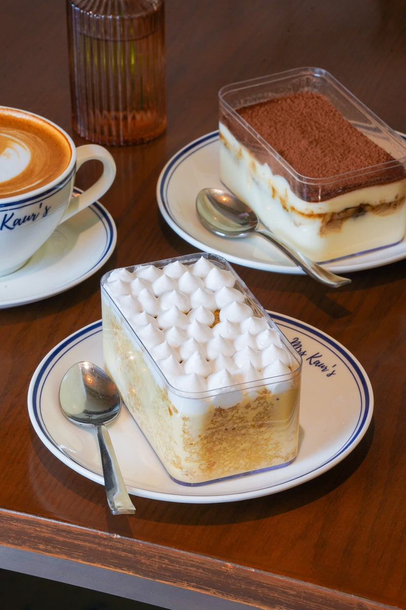 Two desserts and a cappuccino on a walnut table at Mrs Kaur’s